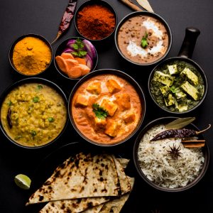 A delicious spread of North Indian vegetarian dishes, featuring dal, curry, rice, naan, and spices on a dark surface.